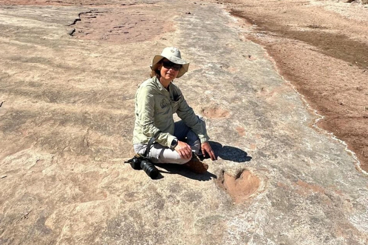 Guest sitting beside a large dinosaur footprint on a rocky riverbed during a day trip from Mhara River Camp, Zimbabwe